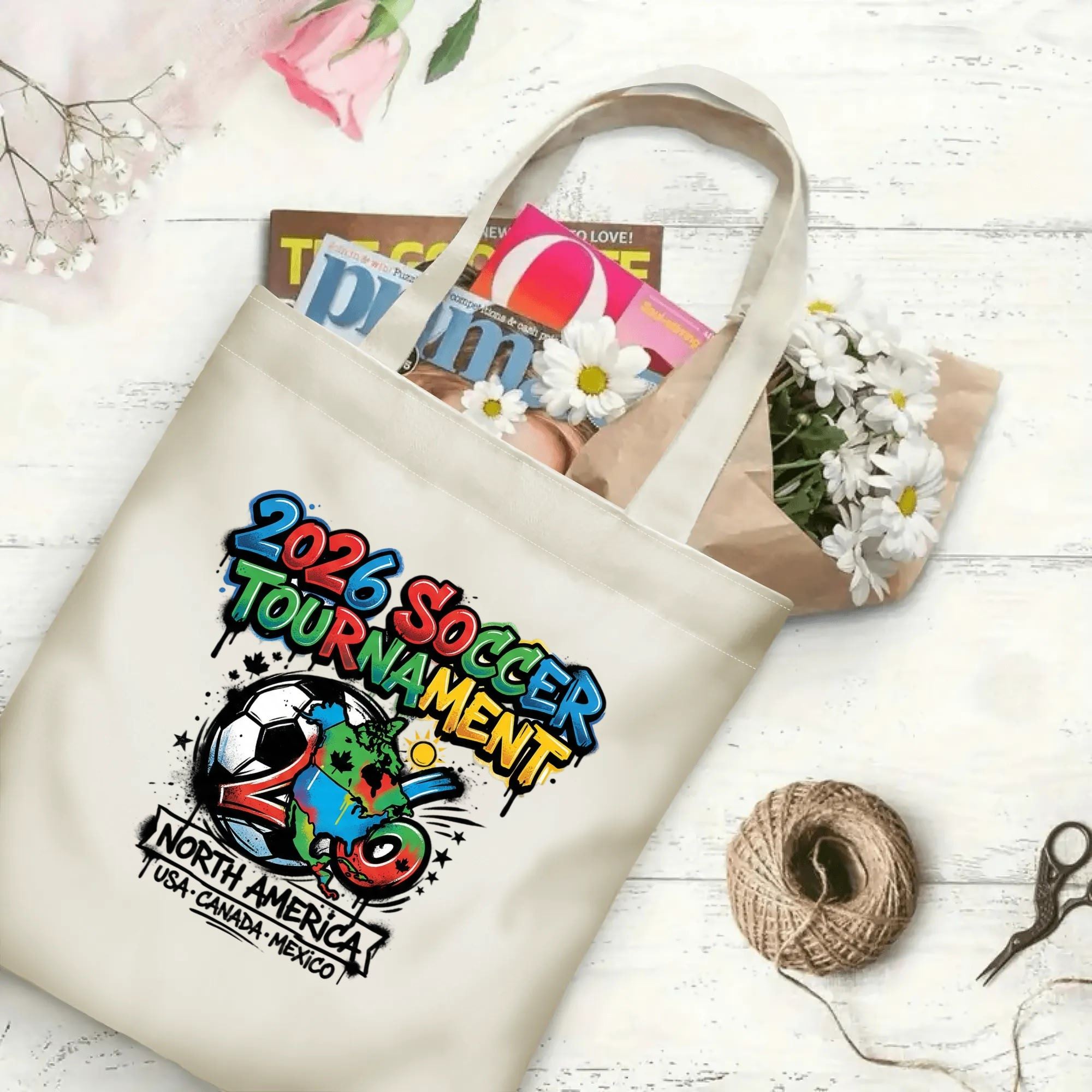 Color spray drip continent map soccer graphic canvas tote bag laid flat with magazines and daisies, reusable street-style sport fan daily shopping bag