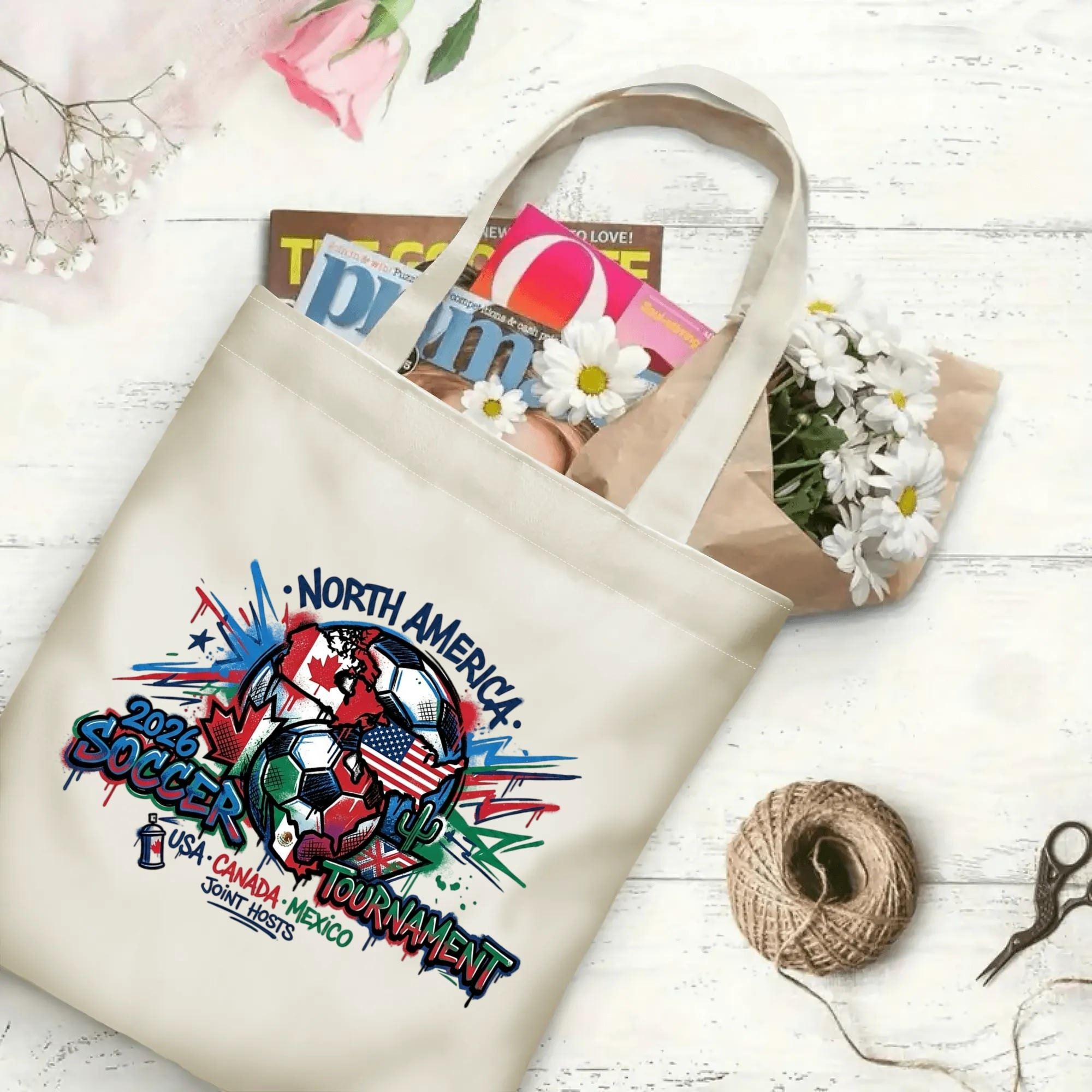 Splash spray paint flag globe soccer graphic canvas tote bag laid flat with magazines and daisies, reusable urban sport fan daily shopping bag