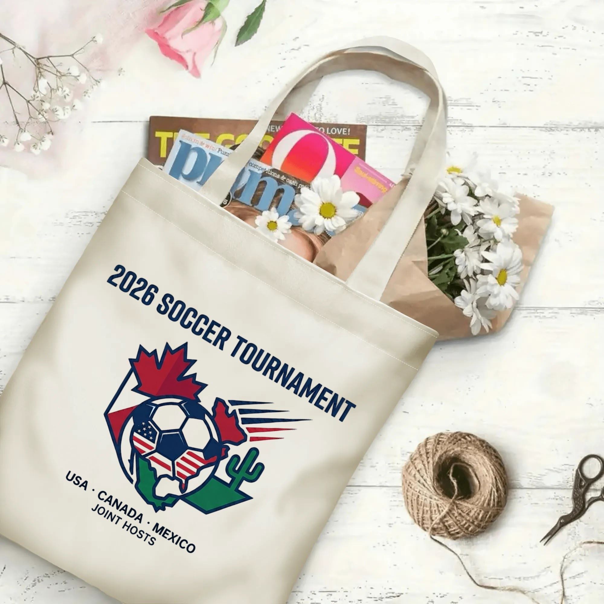 Clean line art shield soccer graphic canvas tote bag laid flat with magazines and daisies, reusable subtle sport fan daily shopping bag