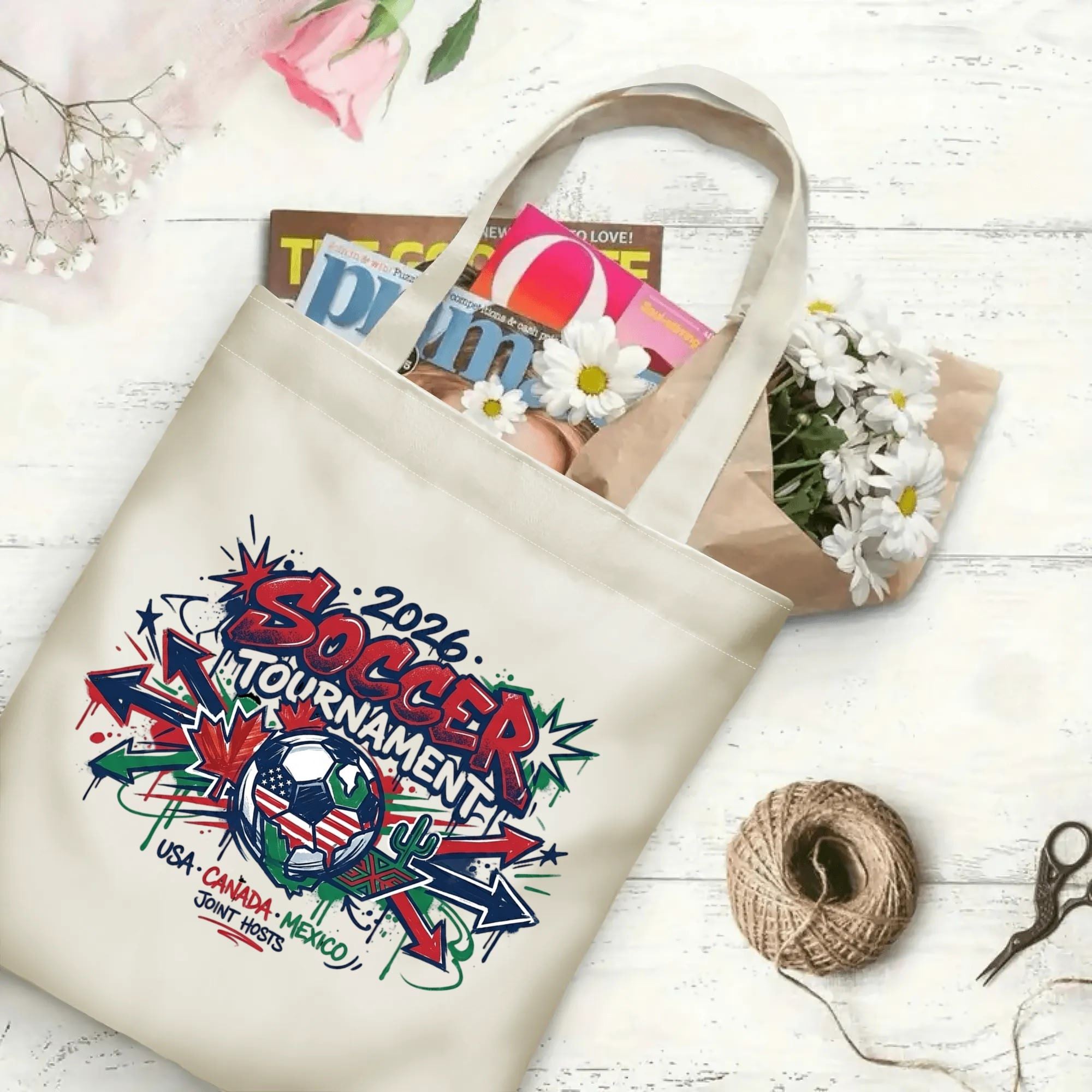Splash arrow graffiti soccer graphic canvas tote bag laid flat with magazines and daisies, reusable sport fan daily shopping bag