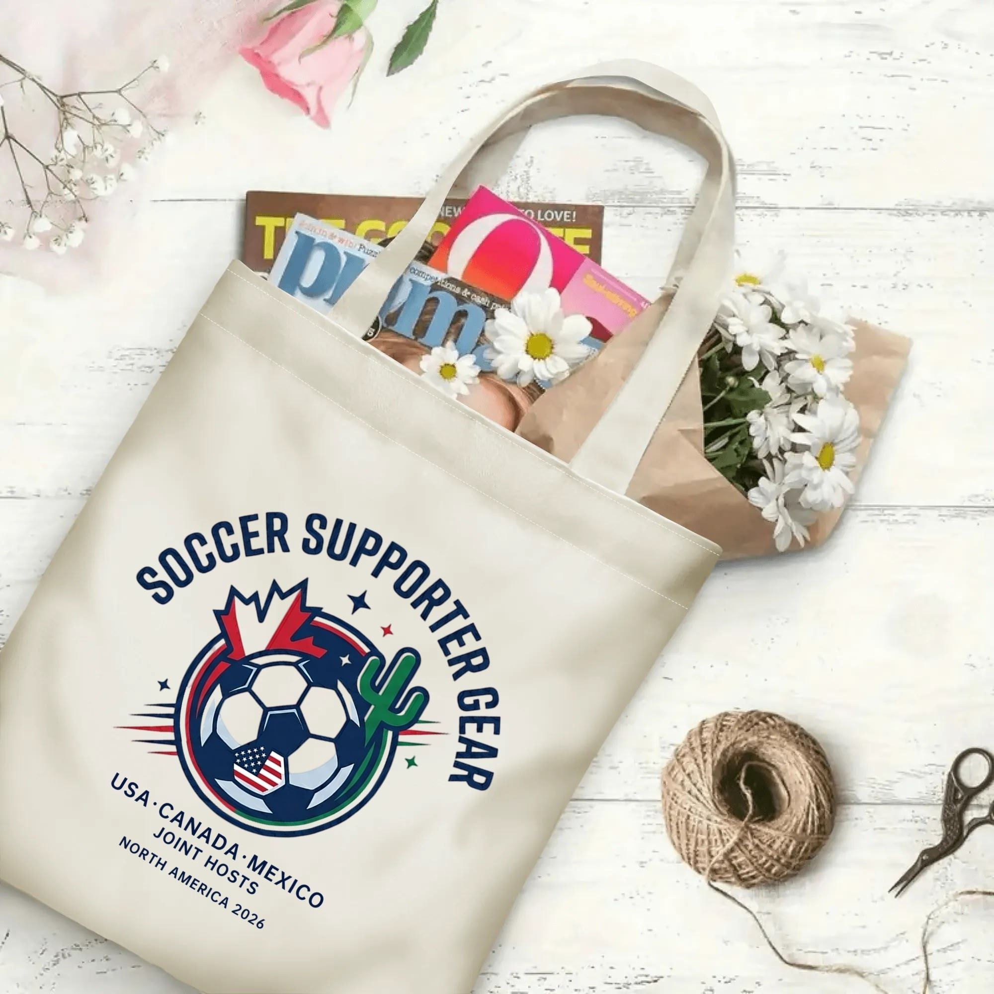 Retro arched varsity soccer crest graphic canvas tote bag laid flat with magazines and daisies, reusable subtle gameday sport fan daily shopping bag