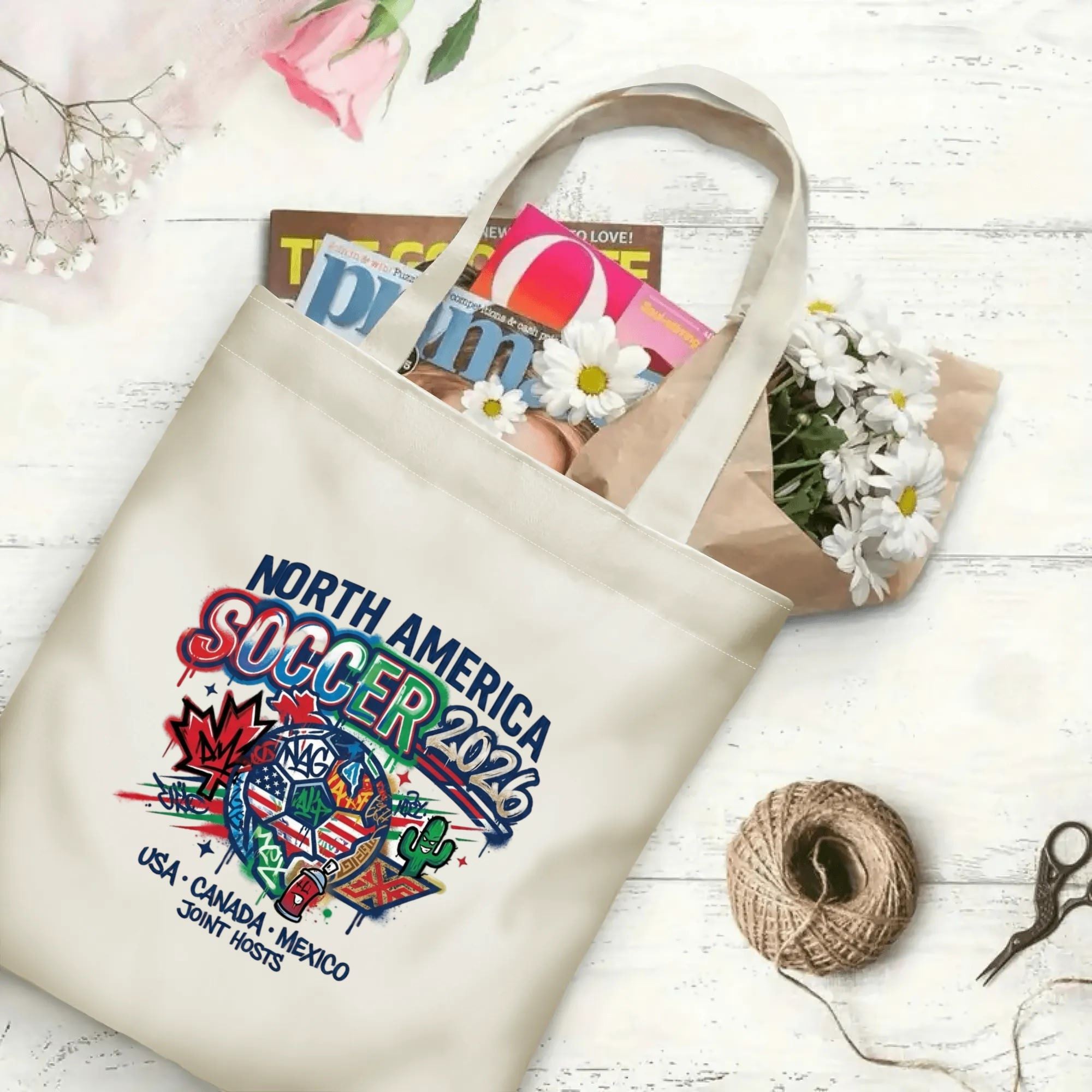 Spray drip street art soccer graphic canvas tote bag laid flat with magazines, daisies and twine, reusable sport fan daily shopping bag
