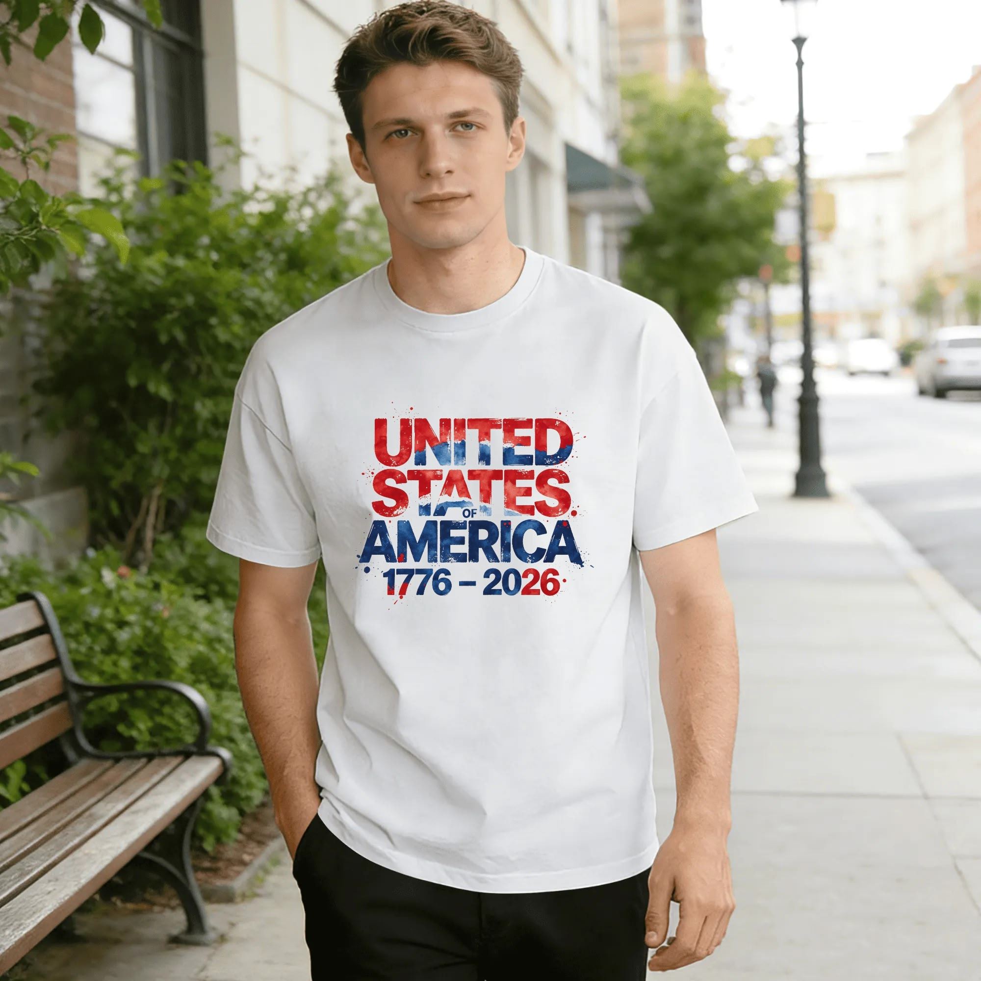 Lifestyle shot of a man wearing the white “USA 1776-2026” watercolor splatter T-shirt, outdoors in an urban setting