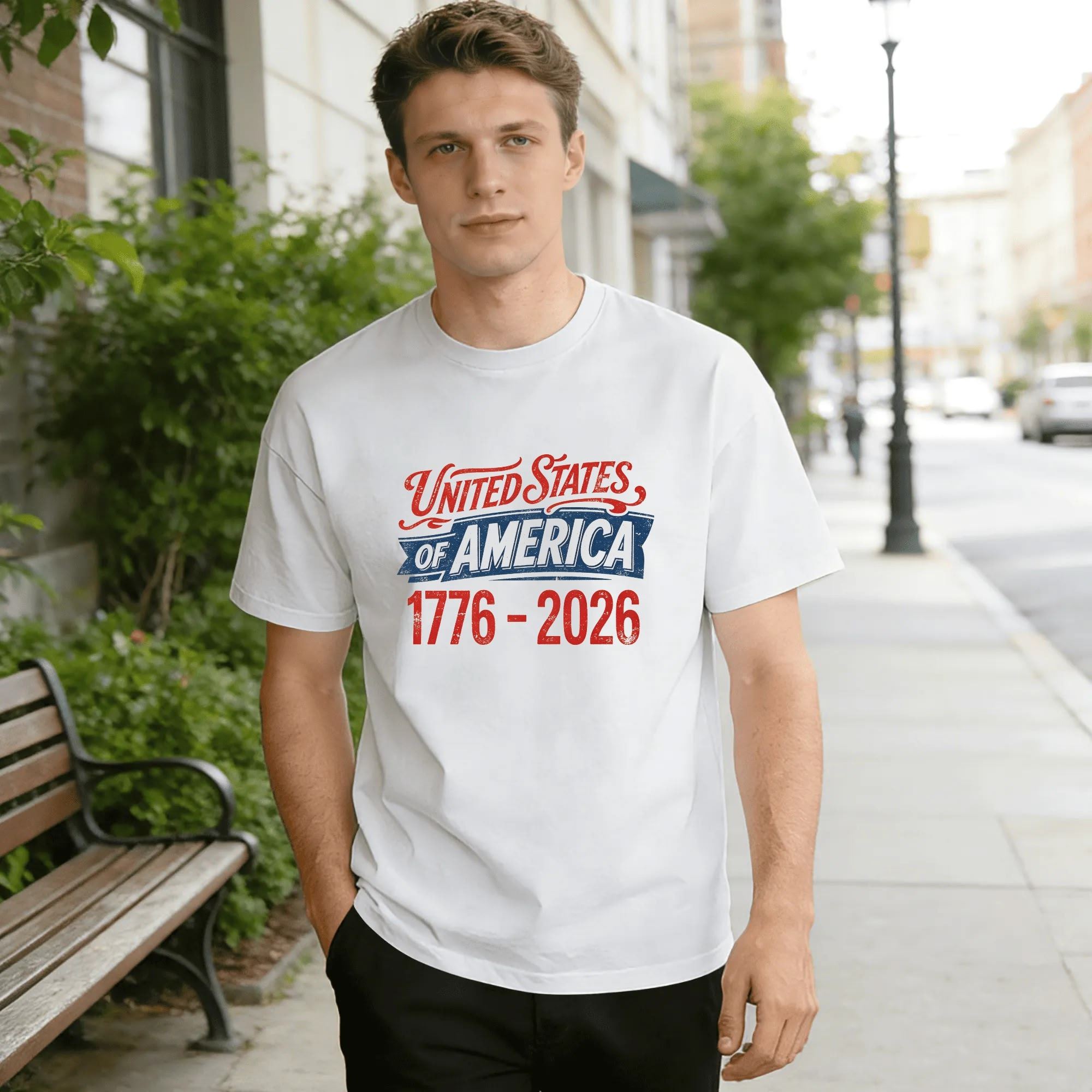 Lifestyle shot of a man wearing the white version of the "United States of America 1776-2026" t-shirt on a city street.