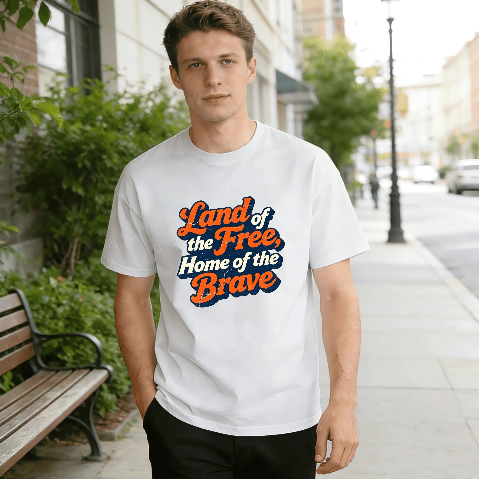 Lifestyle shot of a man wearing the white version of the retro "Land of the Free, Home of the Brave" t-shirt on a city street.