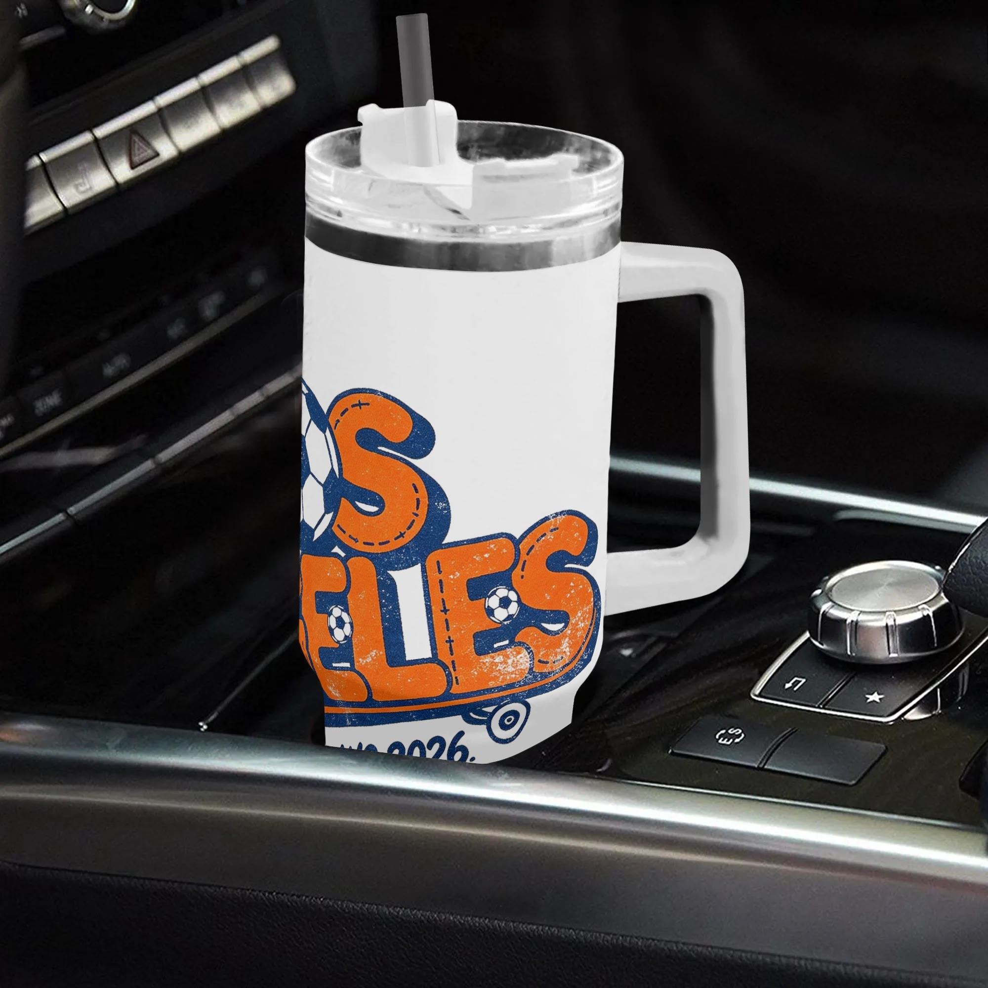 White 40oz insulated tumbler in a car cup holder, featuring a retro skate-style "Los Angeles WC 2026" print with soccer ball lettering in orange and blue.
