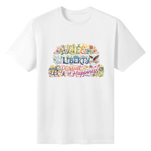 Flat lay of the white T-shirt featuring a vibrant watercolor folk-art print of "Life Liberty Pursuit of Happiness" with flowers, birds, and people motifs.