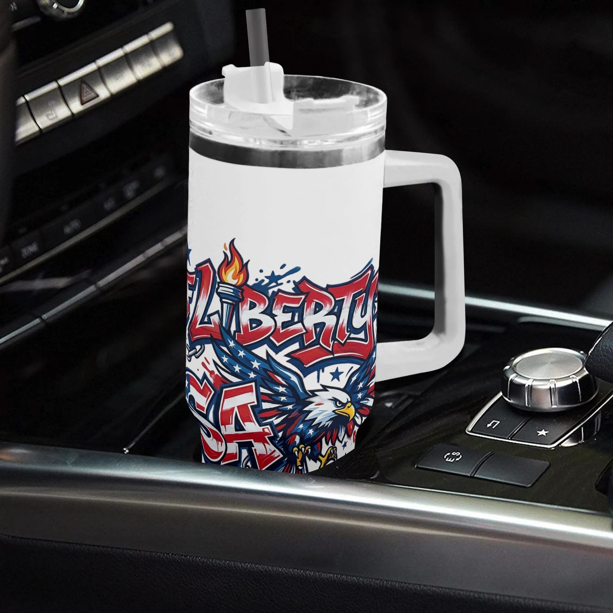 Car interior lifestyle shot: White 40oz insulated handle tumbler placed on vehicle gear console, full wrap street graffiti "Born of Liberty USA" print with bald eagle & Statue of Liberty, patriotic large capacity travel water mug