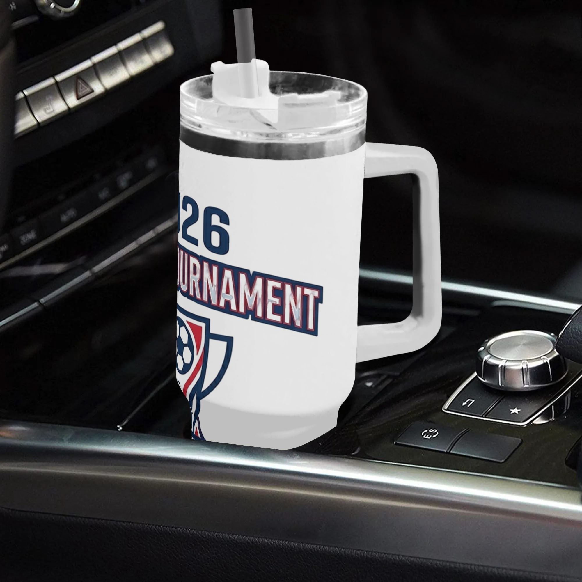 White 40oz handled insulated tumbler printed with 2026 soccer tournament trophy logo, placed on car gear shift console, World Cup fan stainless steel travel mug for driving