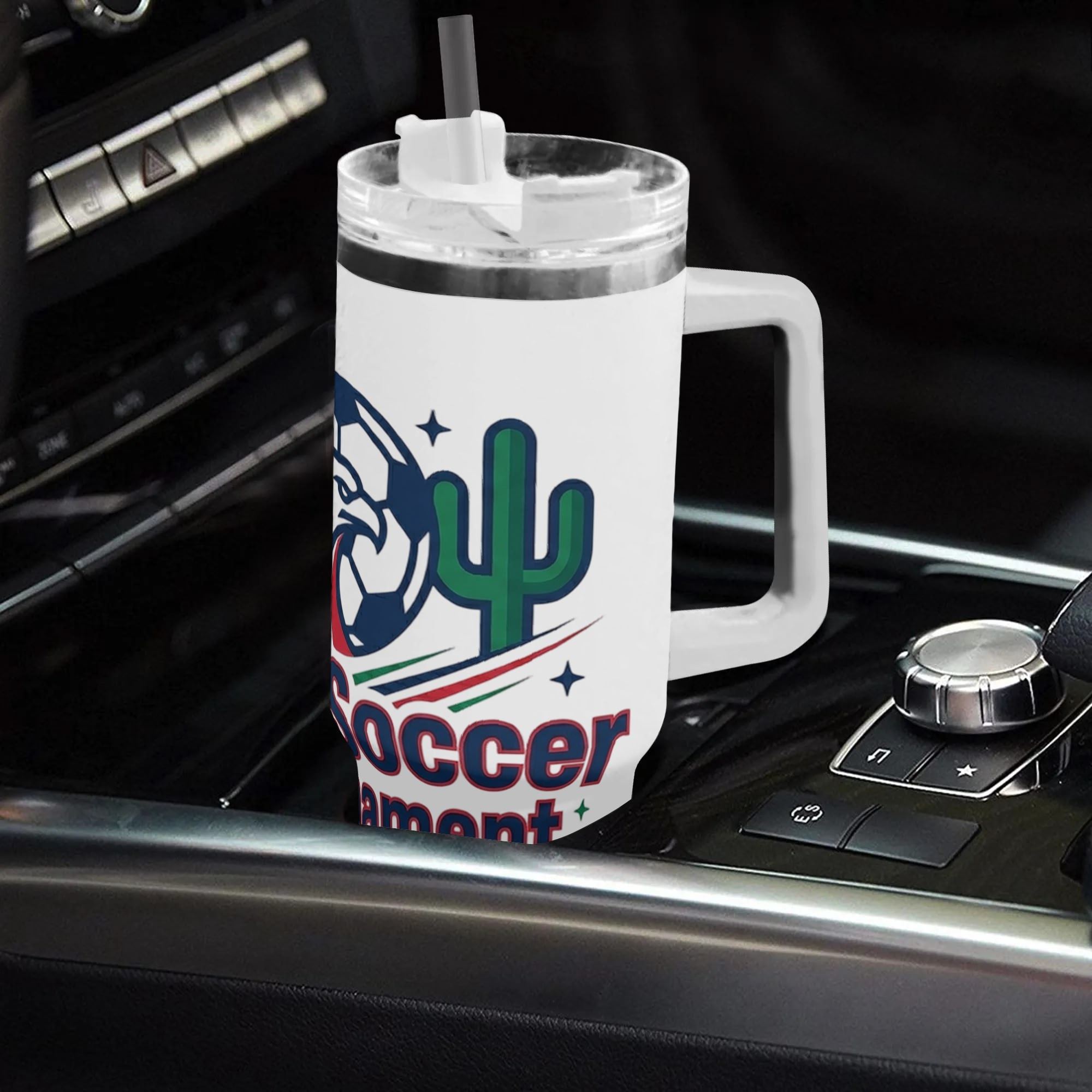 White 40oz handled insulated tumbler printed with eagle maple cactus soccer badge graphic, placed on car gear shift console, 2026 World Cup fan stainless steel travel mug for driving
