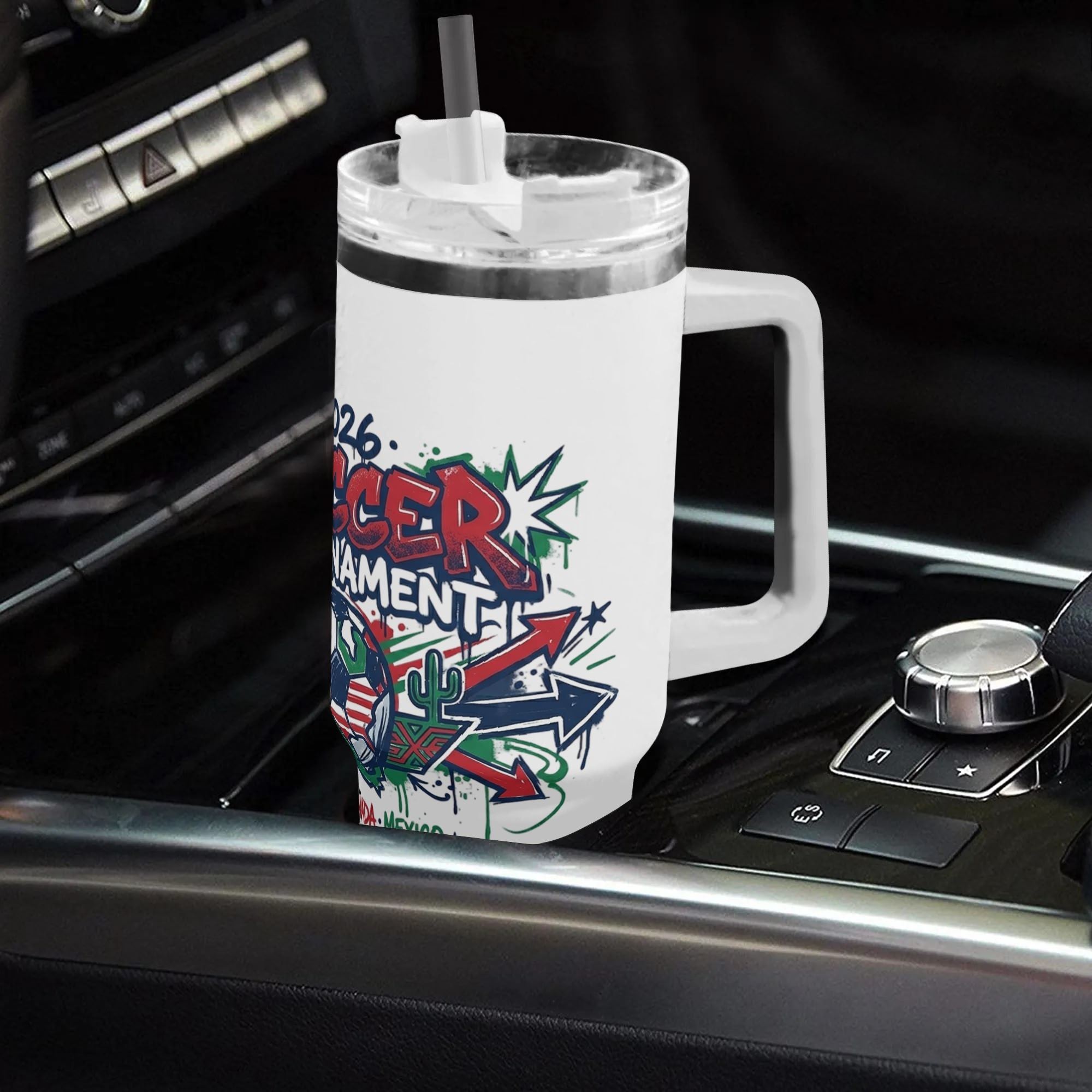 White 40oz handled insulated tumbler with colorful arrow splash graffiti 2026 soccer tournament print placed in car gear shift console, three host patriotic stainless steel travel mug for driving soccer fans