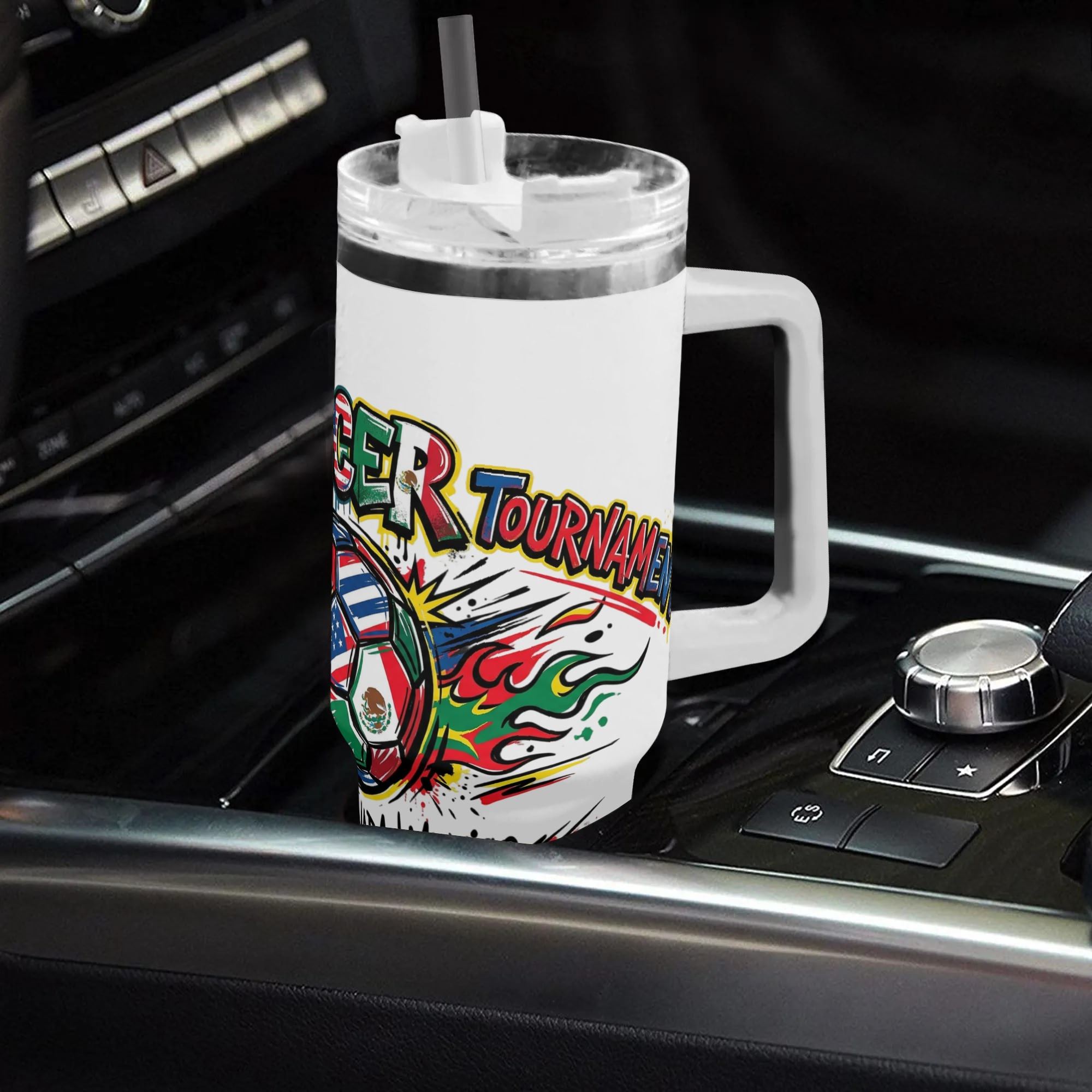 White 40oz handled insulated tumbler with flame graffiti three-flag soccer graphic, placed on car gear shift console, 2026 World Cup fan stainless steel travel mug for driving