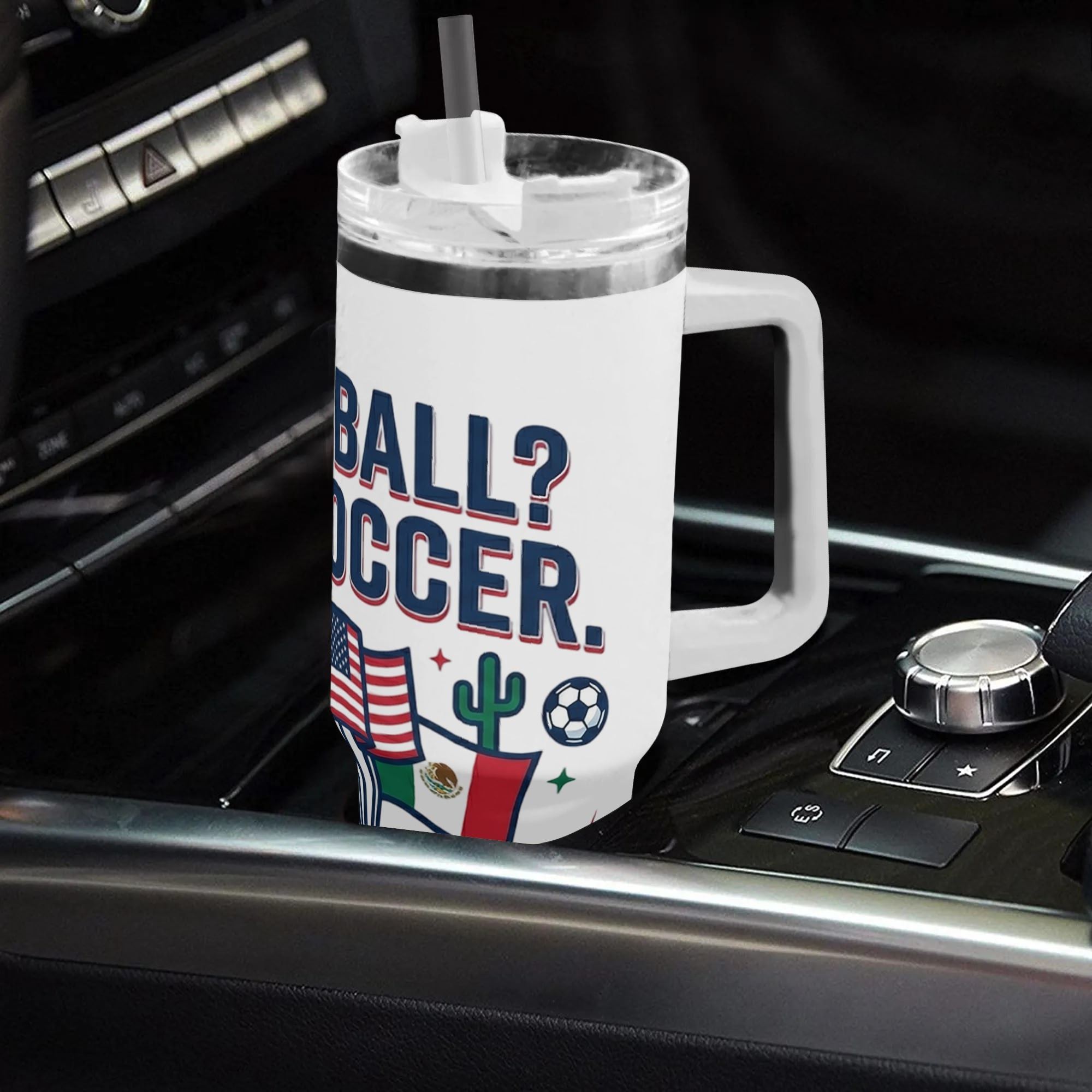 White 40oz handled insulated tumbler printed with "Football? No, Soccer" slogan and US, Canada, Mexico flags, placed on car gear shift console, funny 2026 World Cup fan stainless steel travel mug for driving