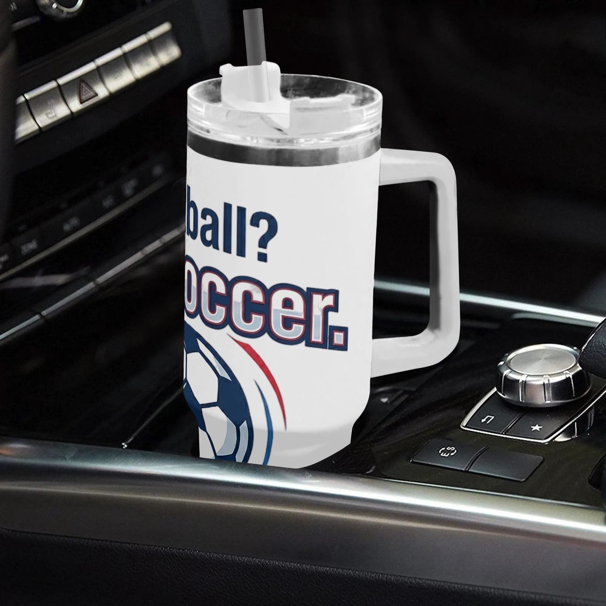 White 40oz handled insulated tumbler printed with "Football? No, Soccer" retro soccer graphic, placed on car gear console, soccer fan stainless steel travel mug for driving use