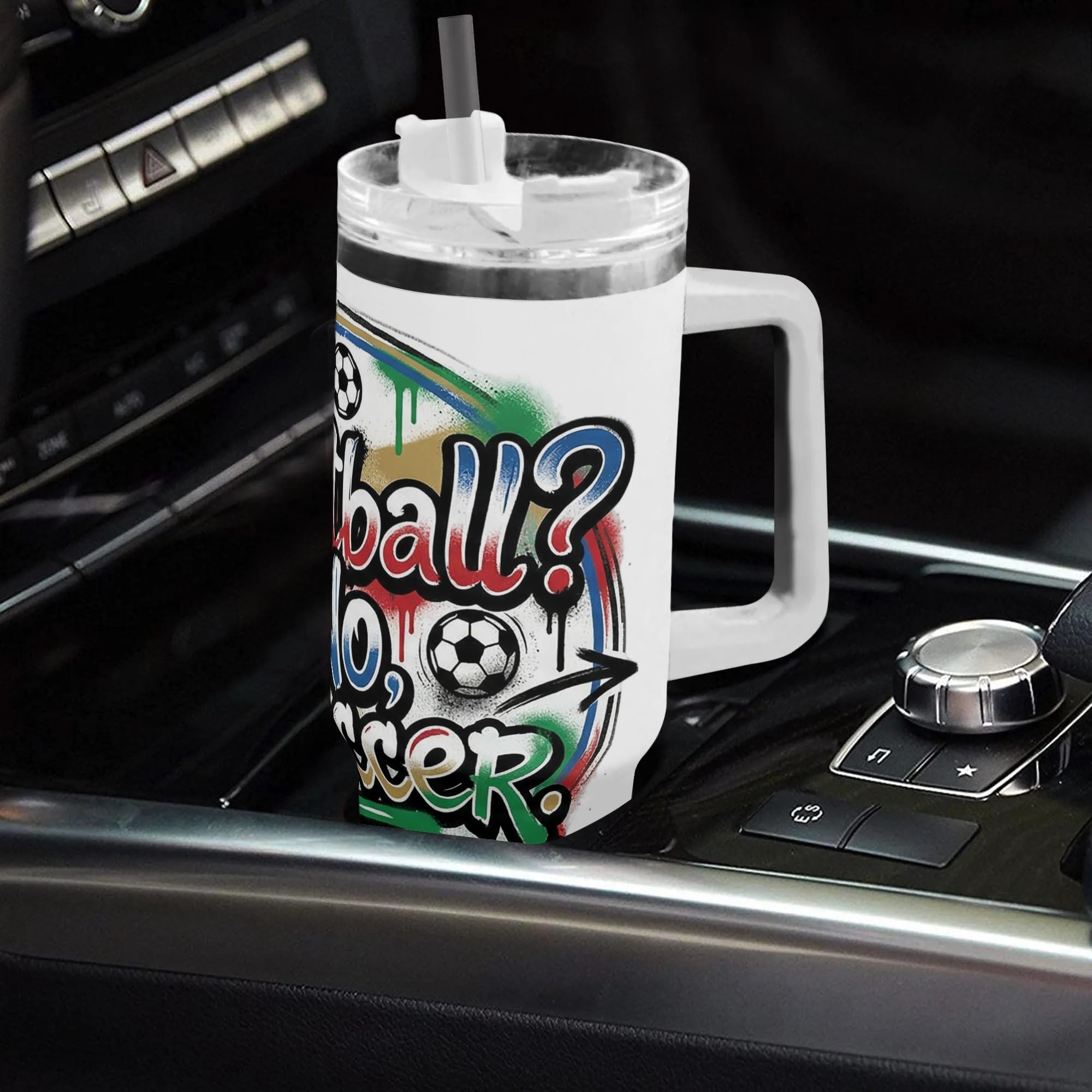 White 40oz handled insulated tumbler with "Football No, Soccer" drip graffiti design, placed on car gear console, soccer fan stainless steel travel mug for driving use