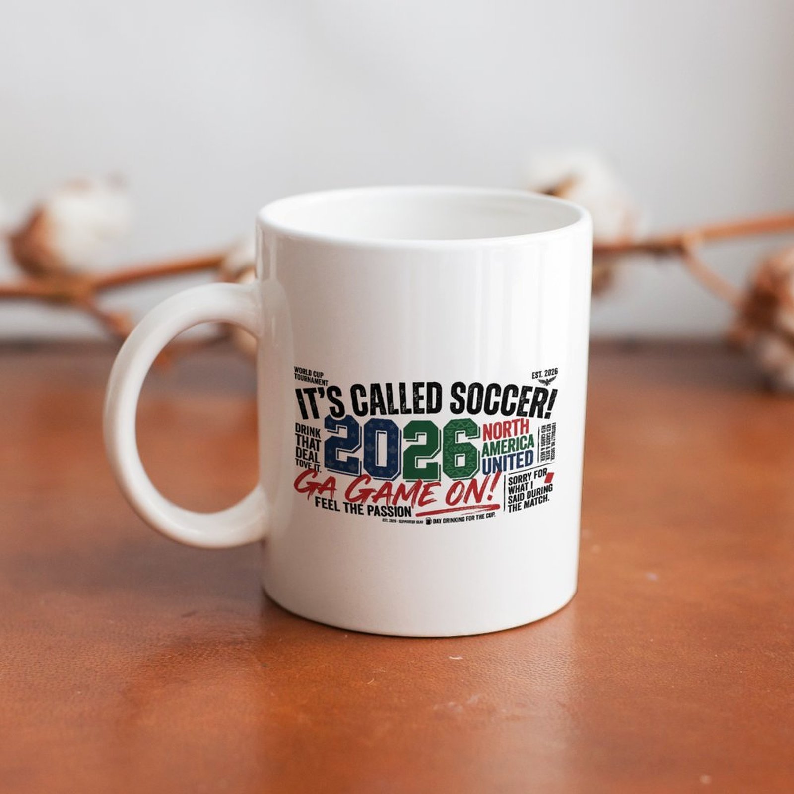 "It's Called Soccer! 2026" mug placed on a wooden table, showing the side view of the print and handle.