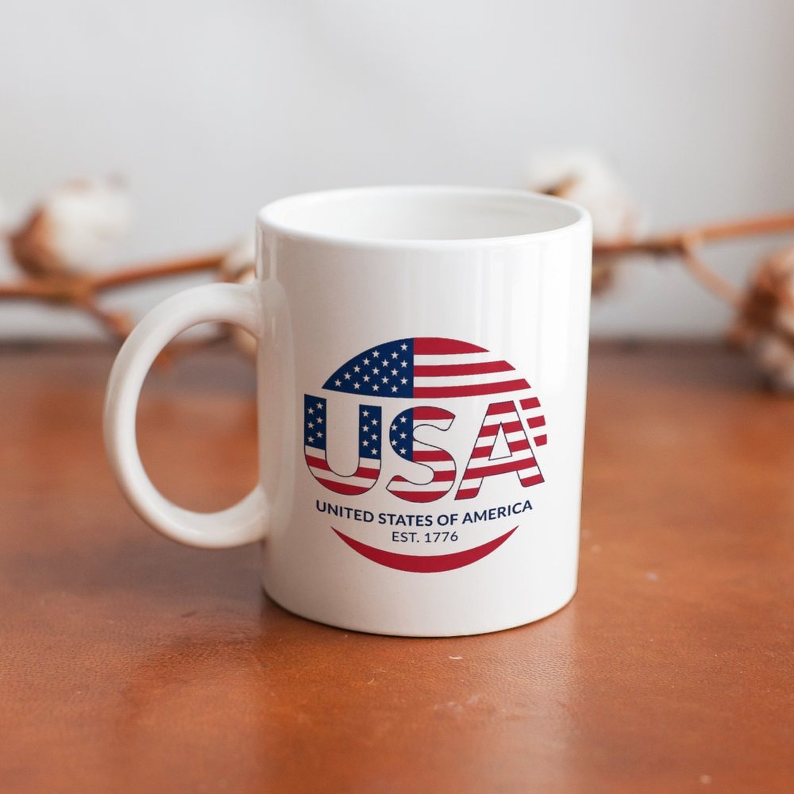 Lifestyle shot: Patriotic USA flag print mug placed on warm wooden table with cotton sprig background for home display