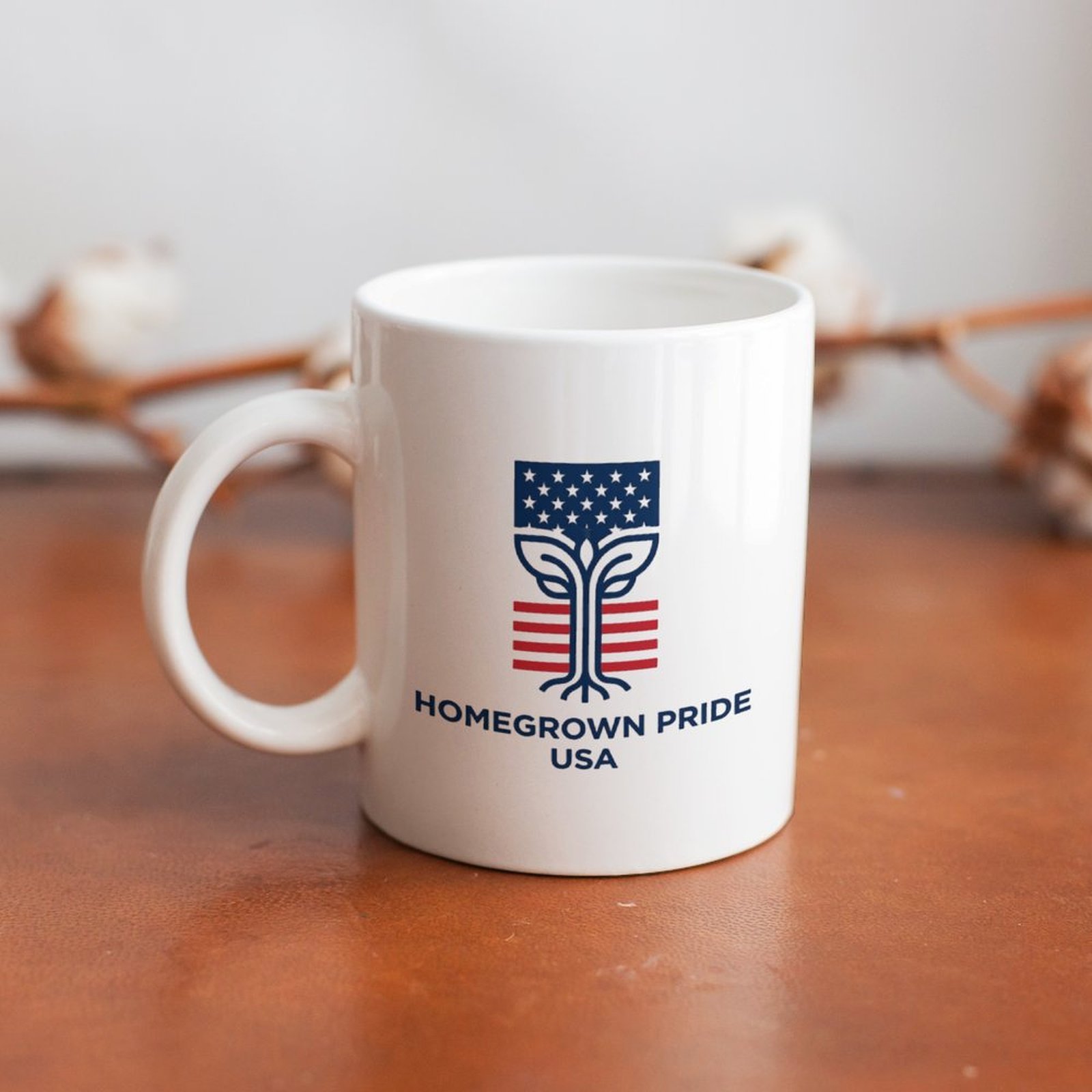 Lifestyle shot: "Homegrown Pride USA" flag tree ceramic mug displayed on warm wooden table with cotton sprig background for home decor