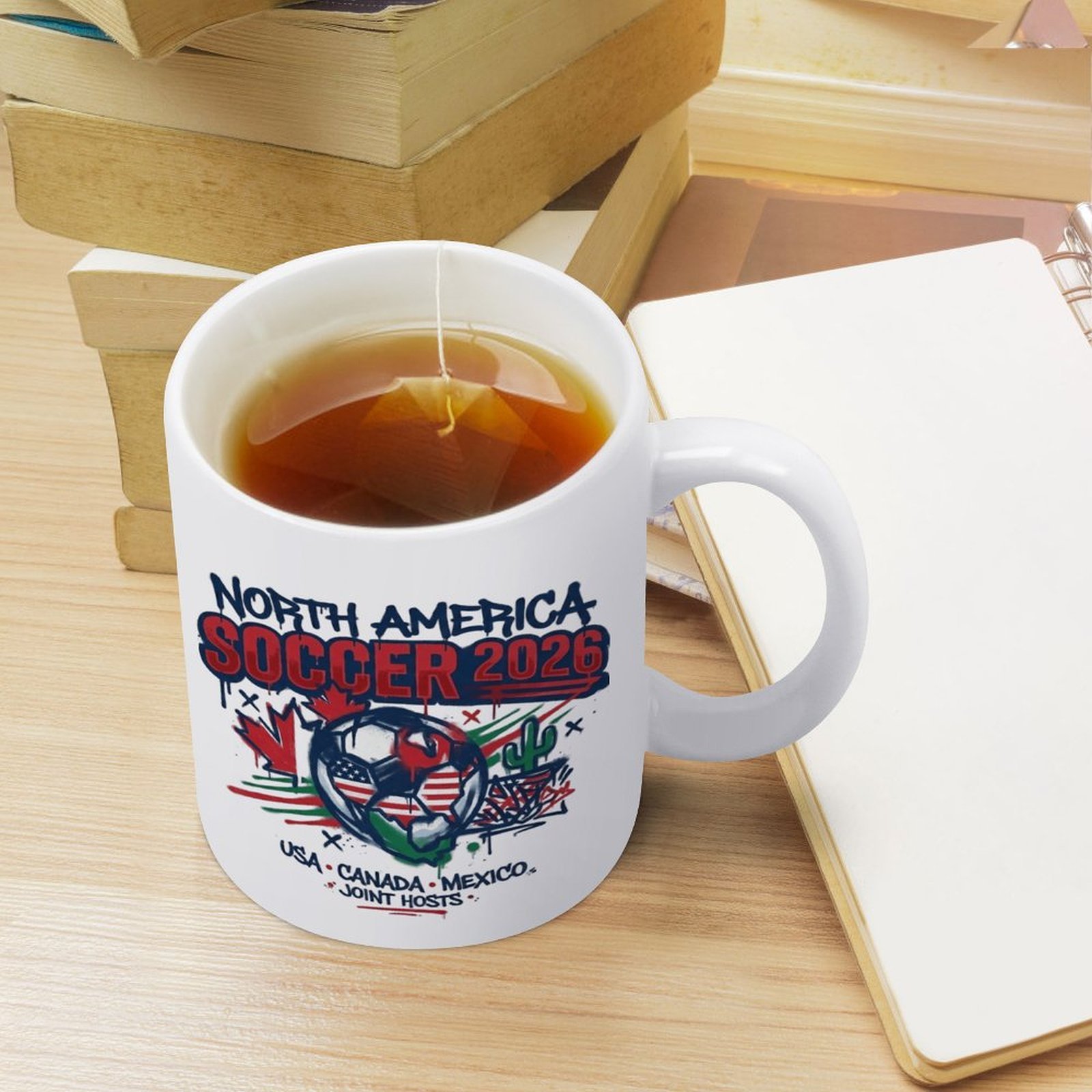 Everyday use scene: the mug with tea on a desk with books and a notebook, showing the graffiti-style 2026 print.